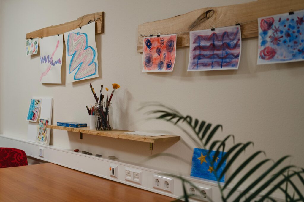Tisch mit Malutensilien vor einer Wand mit bunten Zeichnungen.